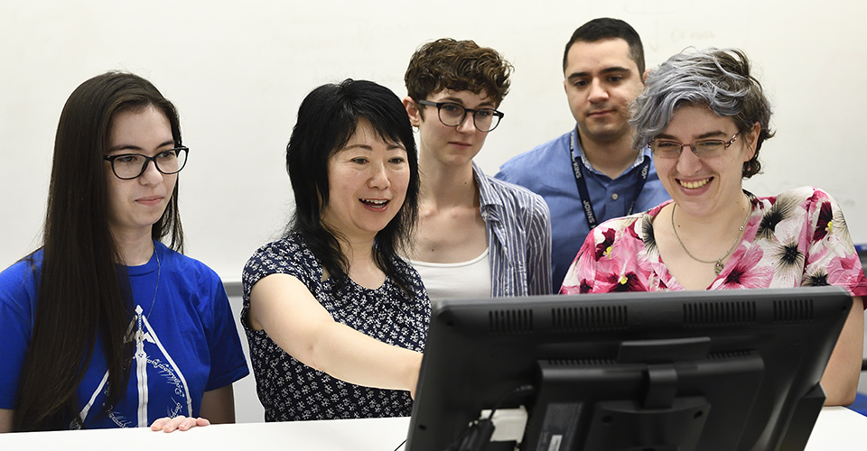 Faculty with graduate students, looking at a computer.