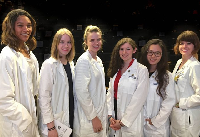 A group of female graduate students stand together with their white coats.