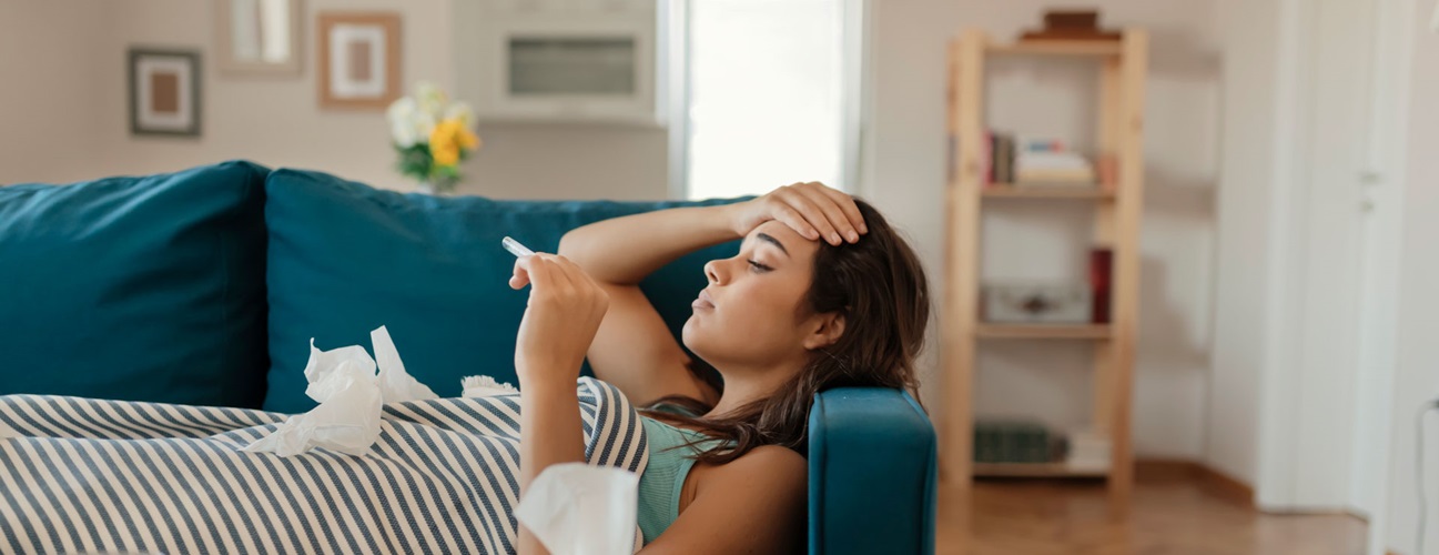 A young woman looks at thermometer after taking her temperature