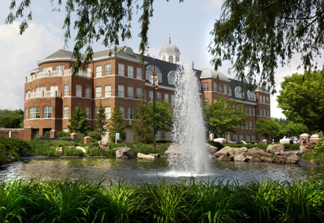 A fountain burbles in the foreground amongst lush landscaping, with Pavilion I at Green Spring Station visible behind it.