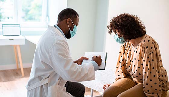 Masked doctor explains procedure to patient in a sunny exam room