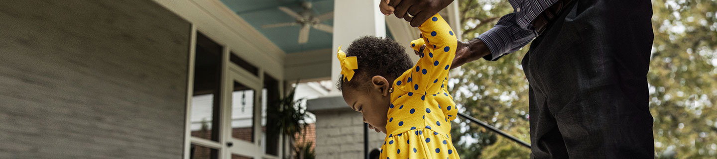 close-up of a toddler with an adult helping her walk