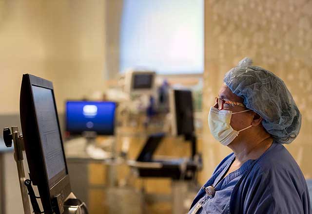 Masked doctor reviewing data on a computer screen.