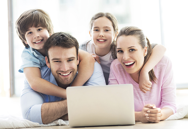 Mother, father and two children lying in front of an open laptop